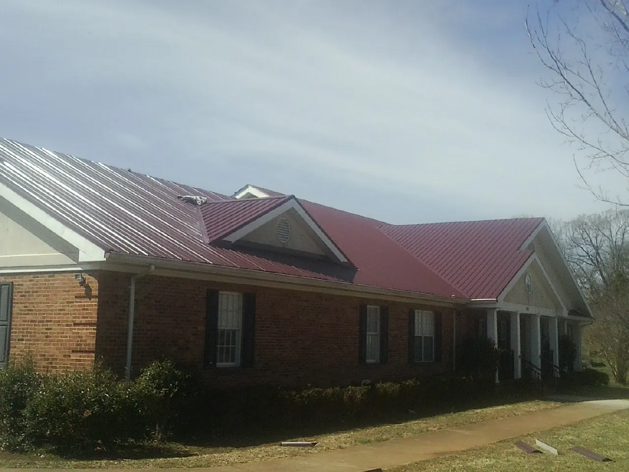 Red metal roof with gabled entries on a long brick building, from a Hail Damage Roof Repair job in Madera