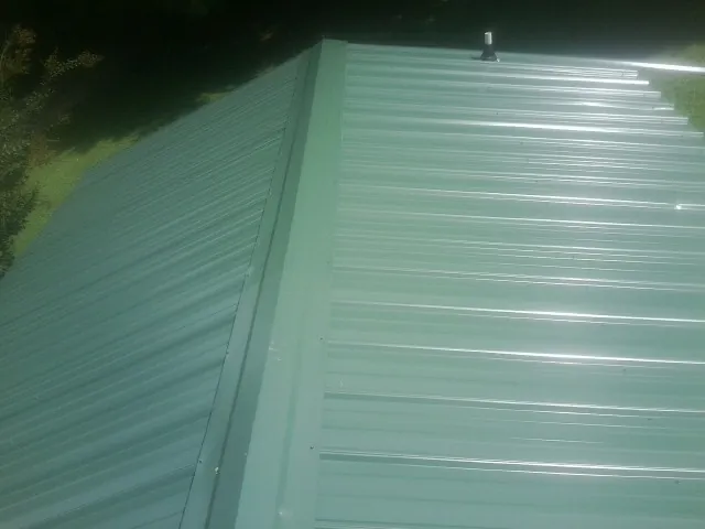New green metal panels meeting at the ridge of a roof — Flat Roof Repair work by our crew in Madera