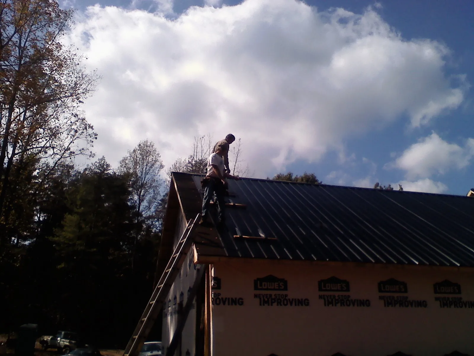 Roofer fastening dark metal panels high against a cloudy sky, from a Roof Inspection job in Madera